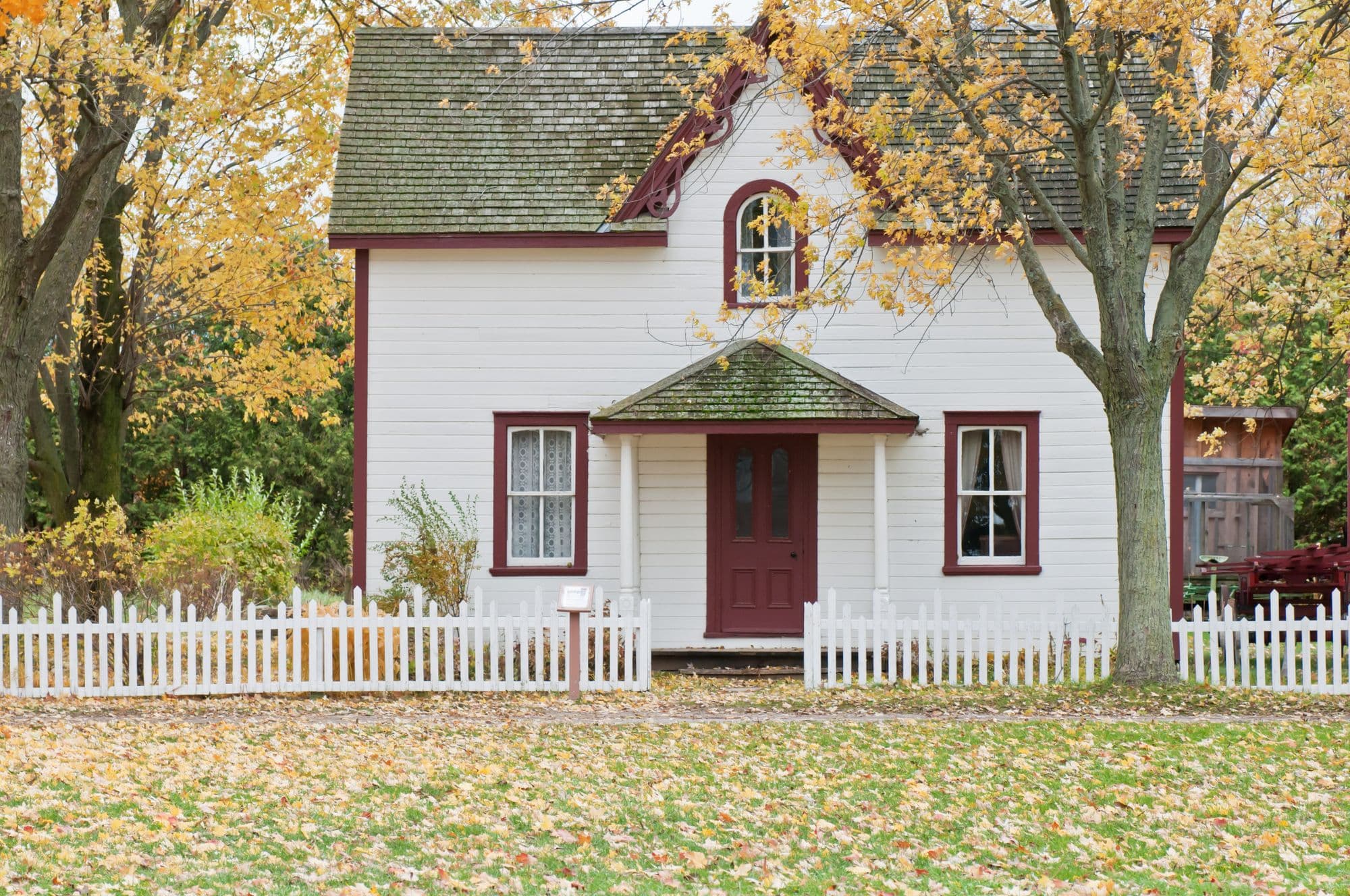 White cottage with a front porch, picket fence, and yard
